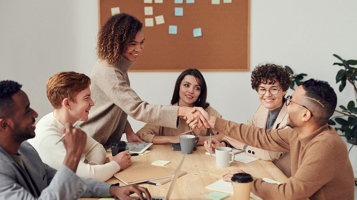 Team sitzt zusammen am Tisch und schüttelt Hände – Moderne Führung