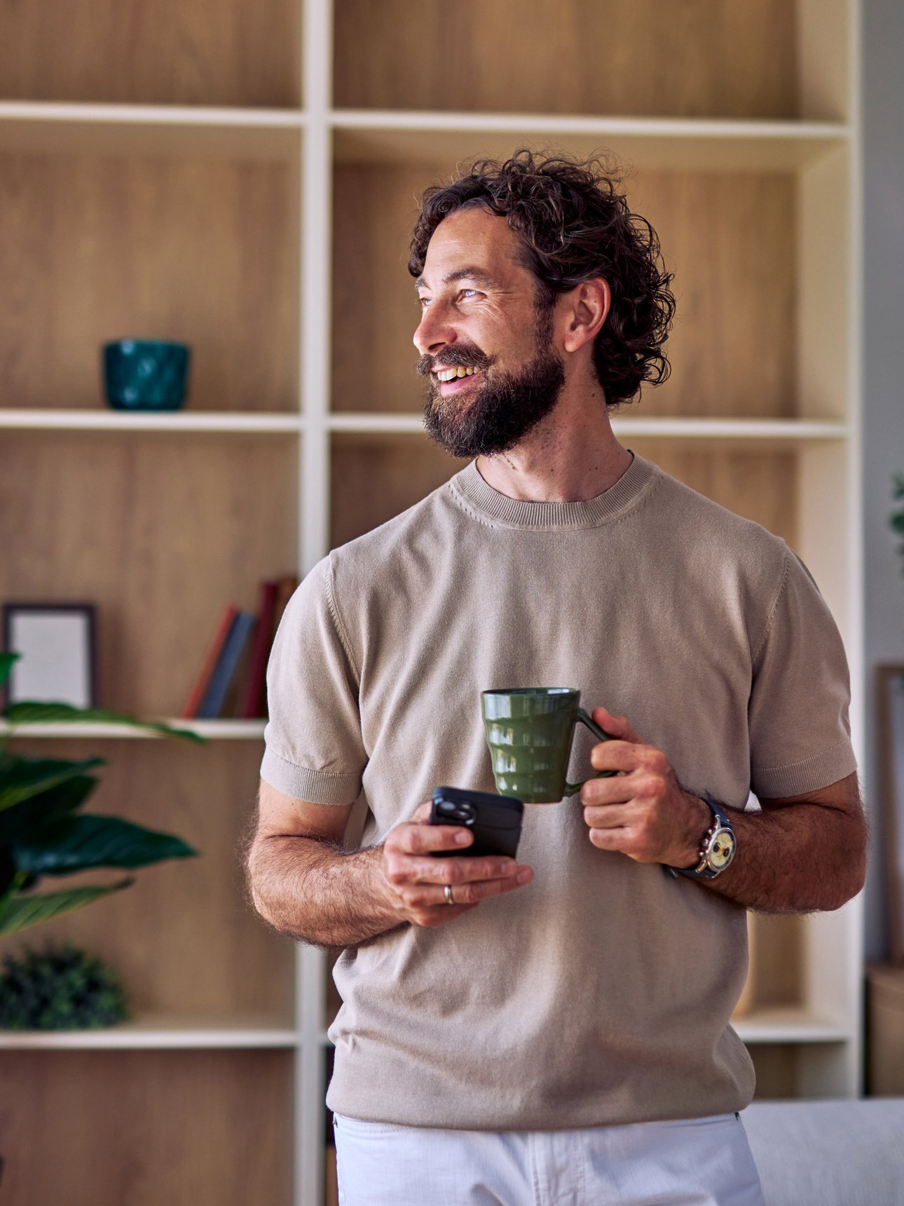 Deine Vorteile Mann steht mit Tasse und Smartphone in seiner Wohnung.