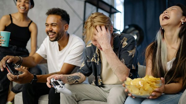 Vier junge Menschen sitzen lachend auf der Couch und spielen ein Videospiel 