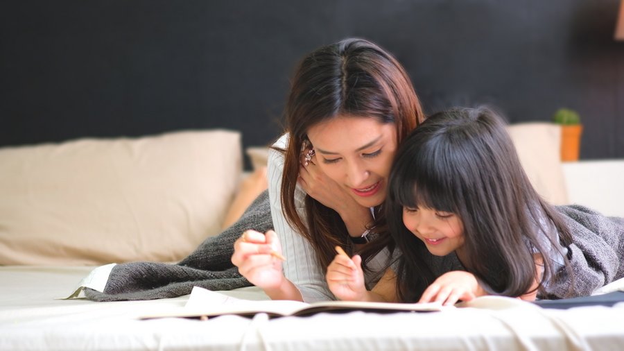 Große und kleine Schwester lesen ein Buch und liegen auf dem Bauch